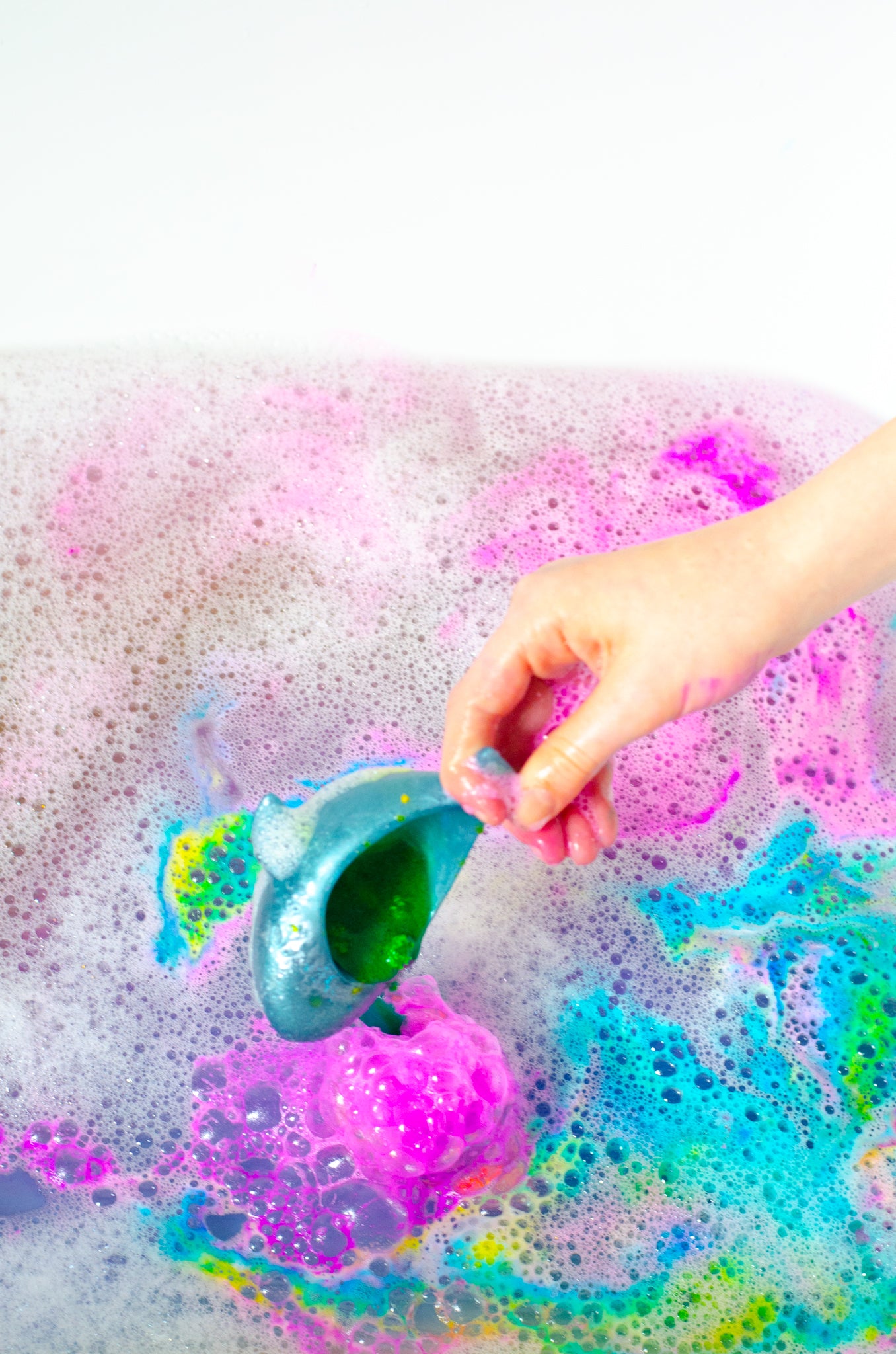 Hand holding a blue toy in colourful potion play for the bath