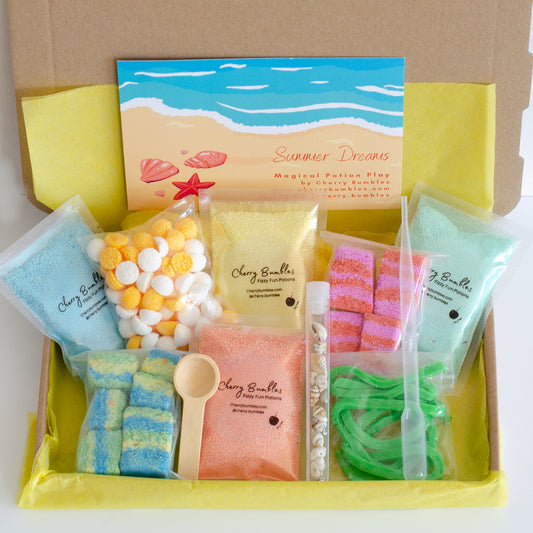 Summer Dreams potion making kit for children, including eight colourful pouches of fizzy and foaming ingredients, shells, pipette and wooden spoon. In a C5 box with yellow tissue paper and instruction card with a beach design on the front.